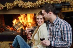A couple drinking wine in front of the fireplace.