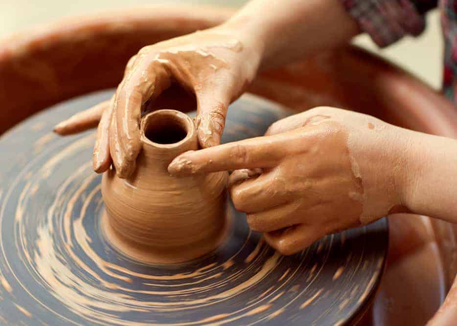 Hands making pottery on a wheel.